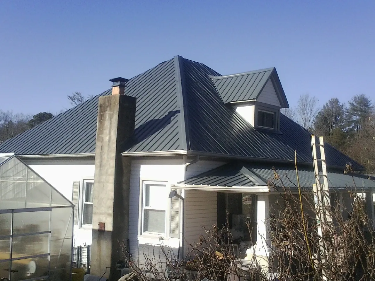 Dark blue standing seam metal roof on a white farmhouse with dormer — Slate & Tile Roof Repair by Roofing Brothers in Glenwood Springs