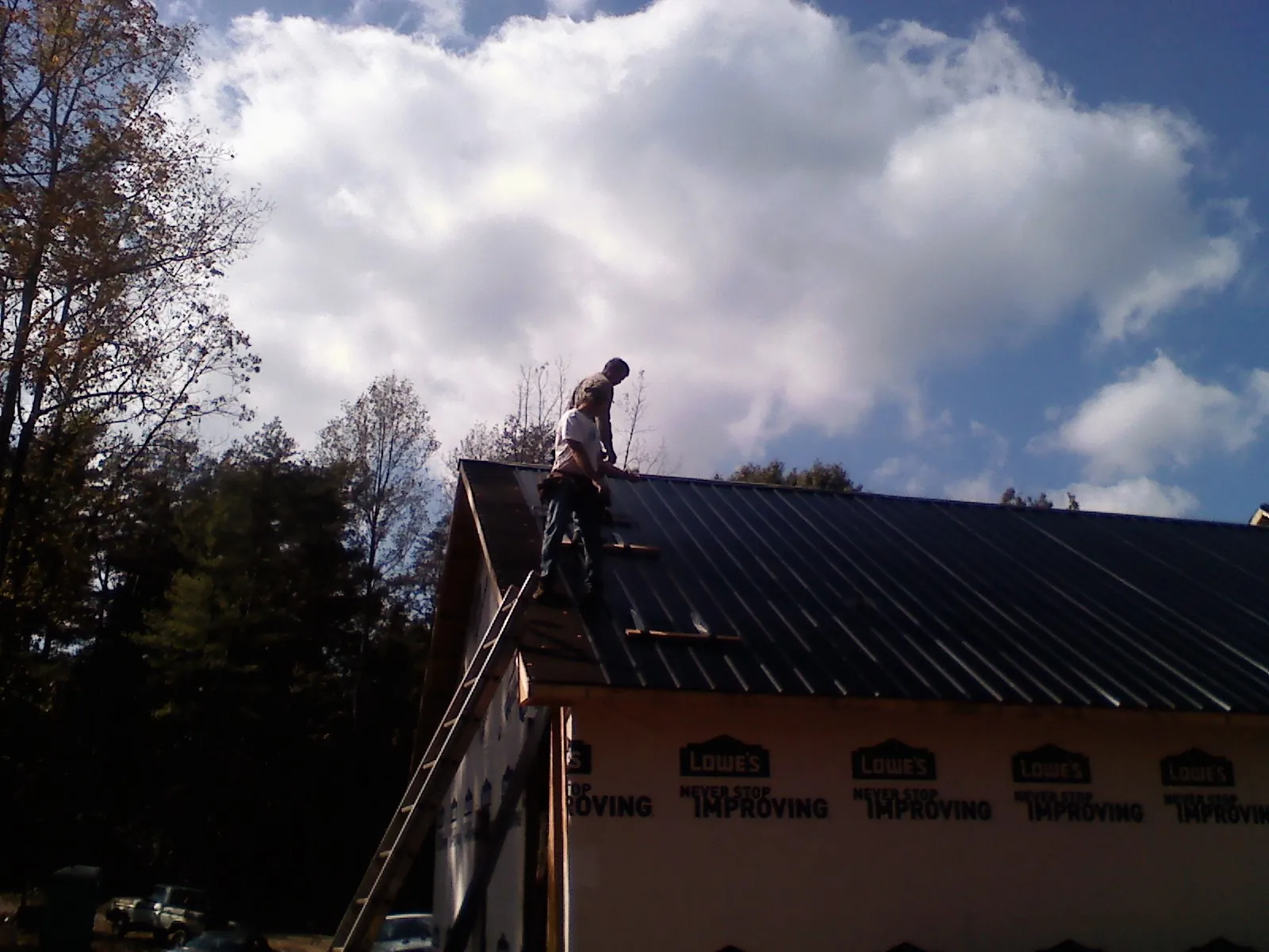 Roofer fastening dark metal panels high against a cloudy sky, from a Roof Inspection job in Glenwood Springs