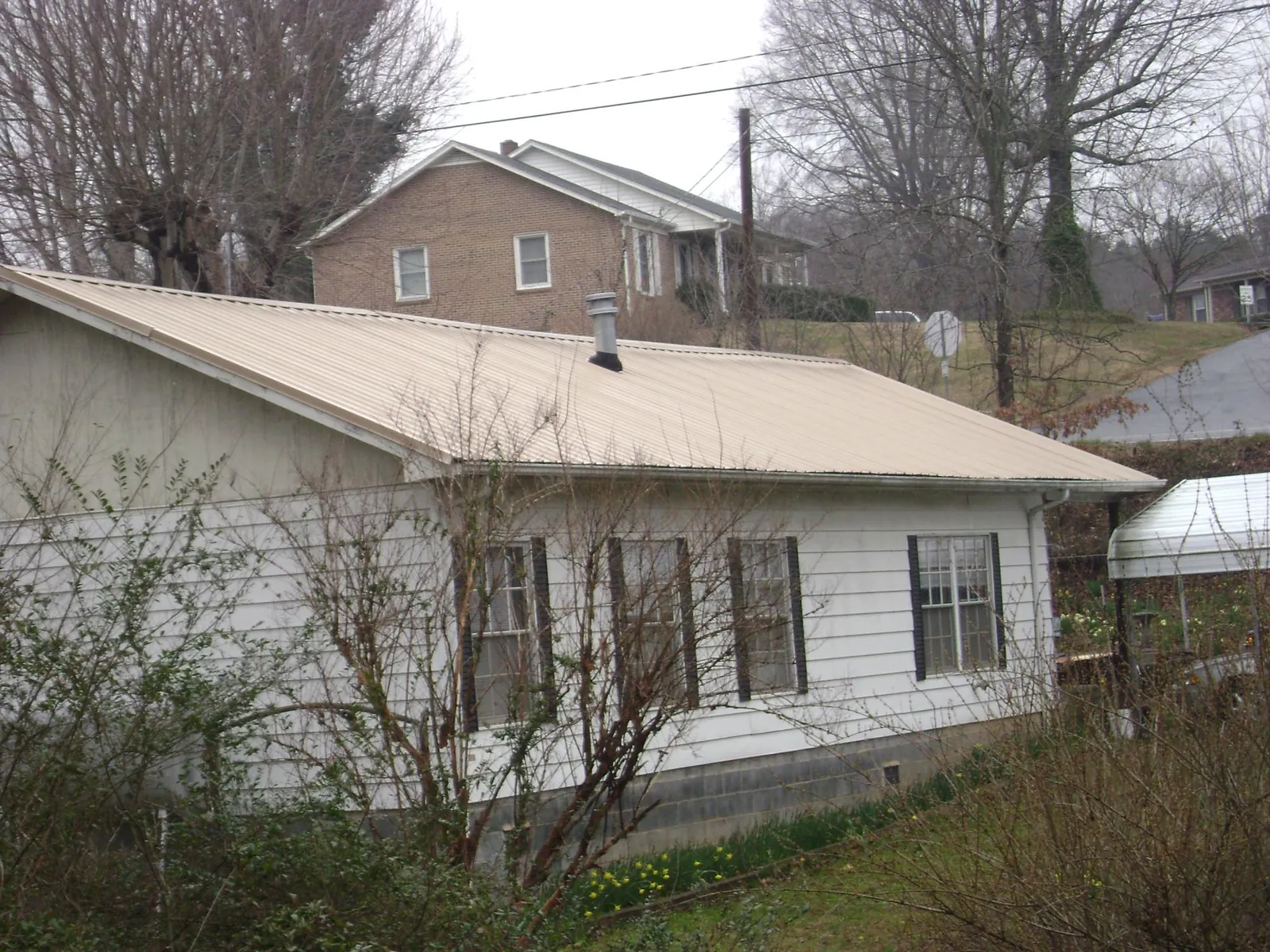 Tan metal roof on a white sided house set into a hillside — Commercial Roofing by Roofing Brothers in Glenwood Springs